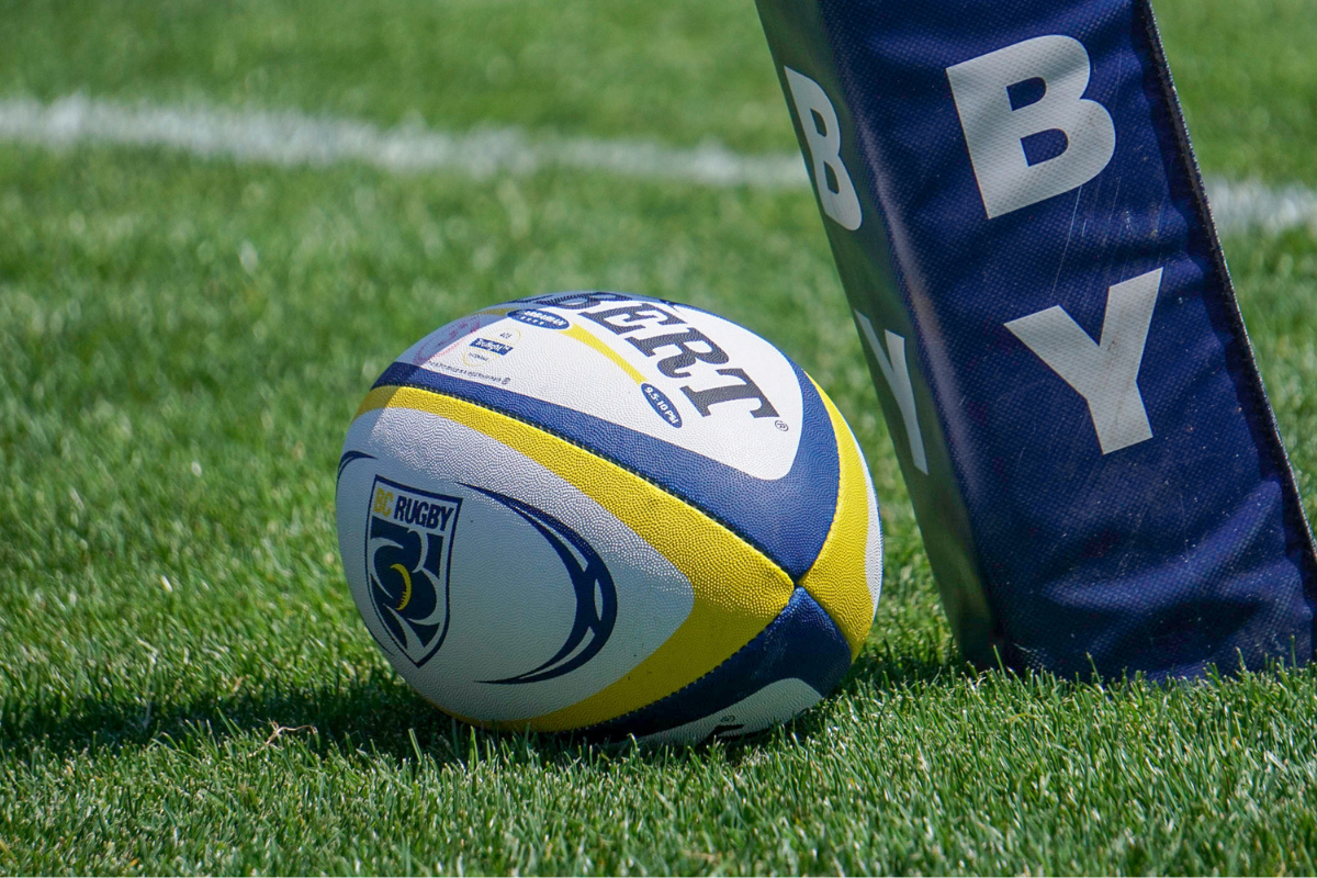 Rugby ball on grass beside a BYU goal post pad