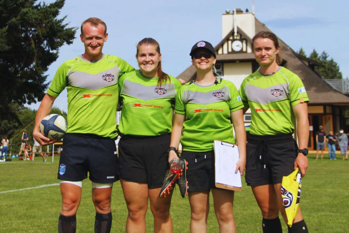 Four people in lime green shirts standing outdoors on a sports field, smiling and posing with race gear.