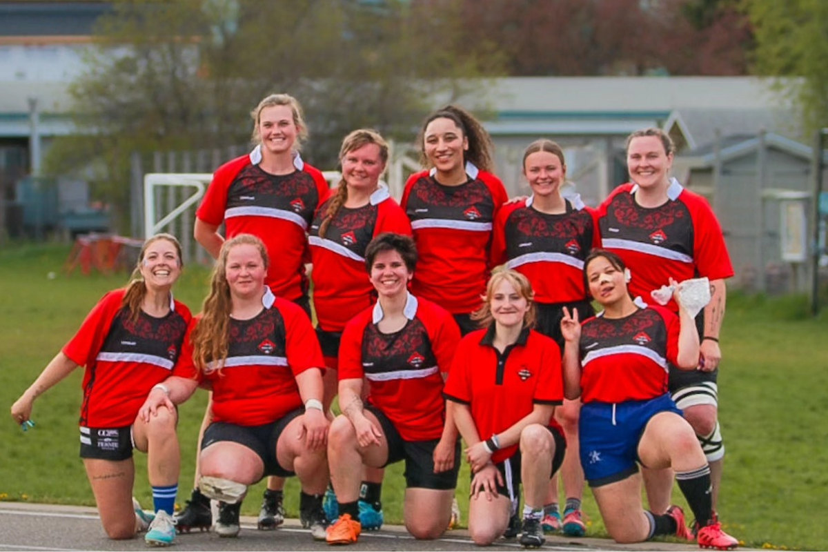 Group of soccer players in red jerseys posing on a field, smiling for a team photo