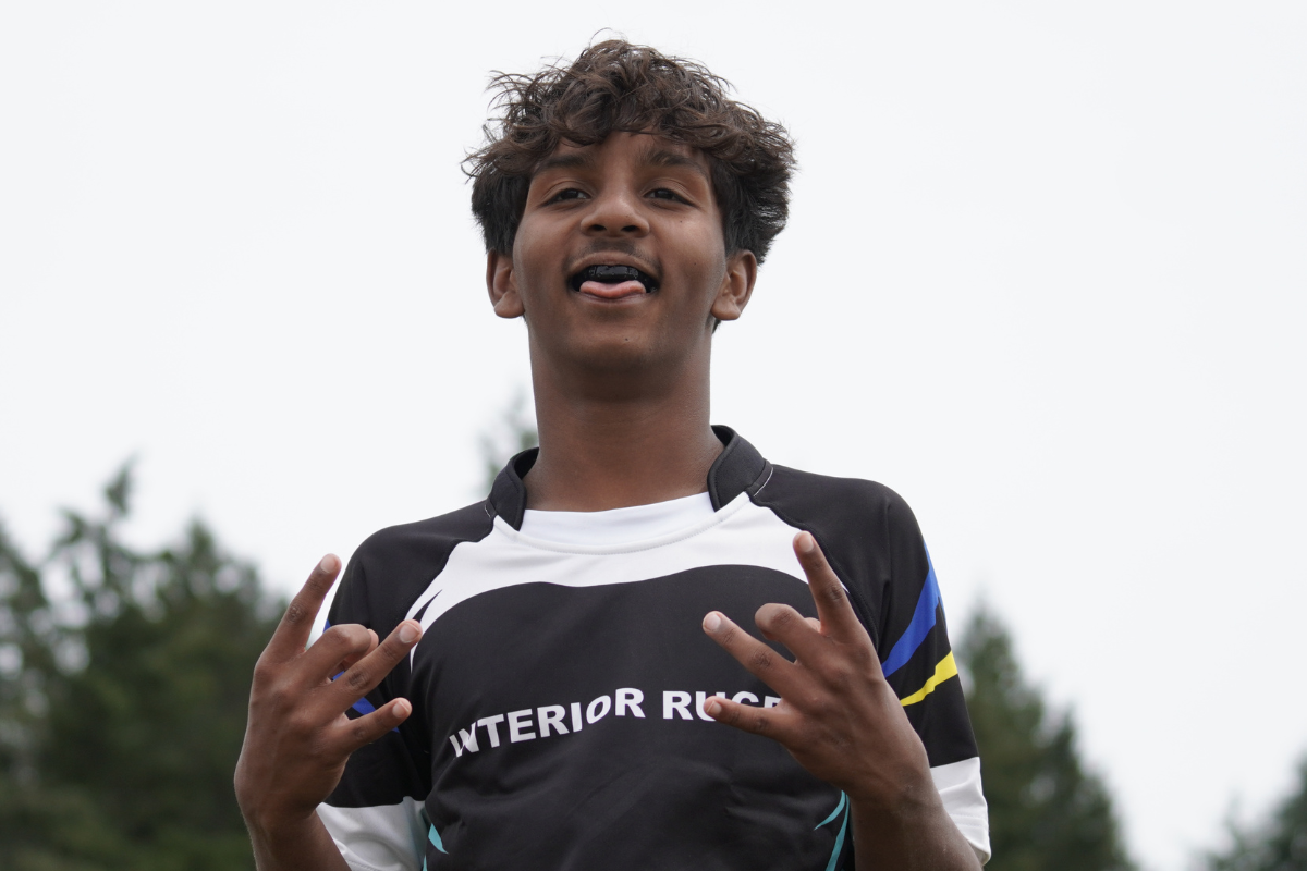 Smiling athlete in a black and white jersey gesturing with both hands outdoors