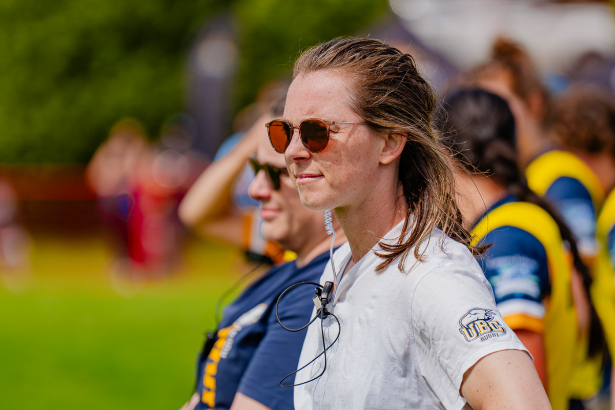 Woman in sunglasses standing on a sports field with other players in the background
