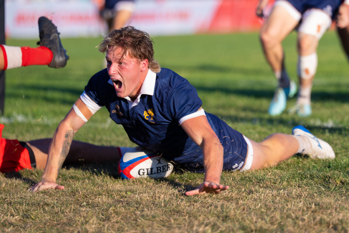 Rugby player in blue jersey diving to score a try on a muddy field during a match