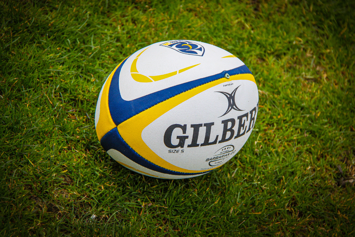 Yellow, blue, and white Gilbert rugby ball on grass