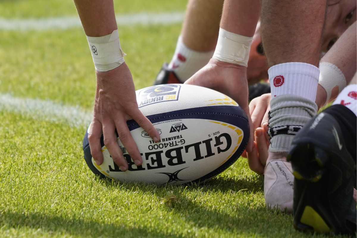 Rugby ball on grass as players’ hands and cleats line up for a scrum close-up