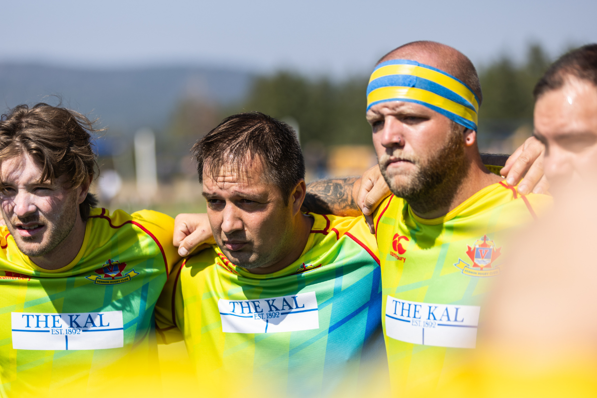 Three muddy runners in bright yellow shirts on a field, focused before a race