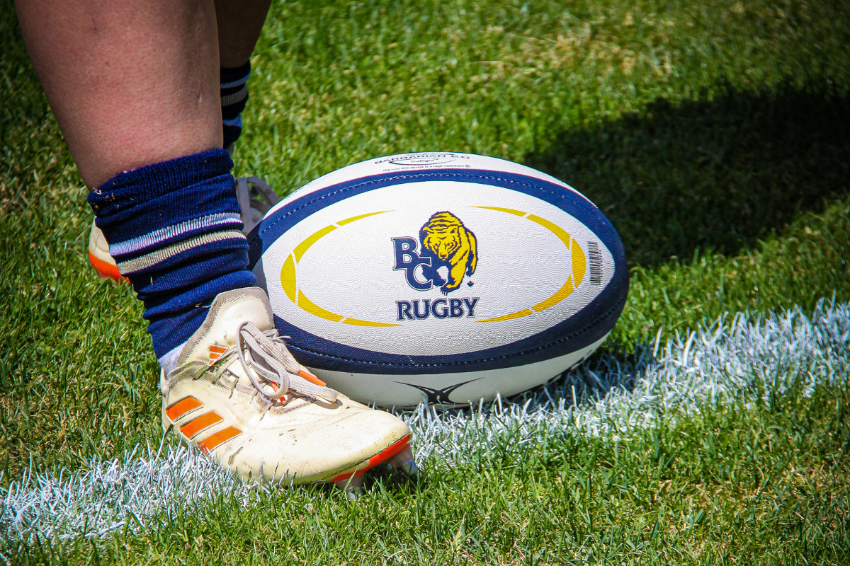 Rugby player’s foot beside a rugby ball on the grass near the sideline