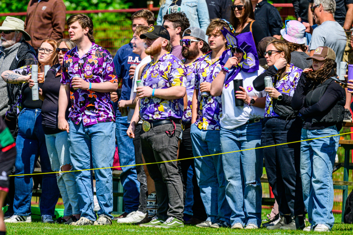 People in purple shirts standing behind a rope barrier at an outdoor event