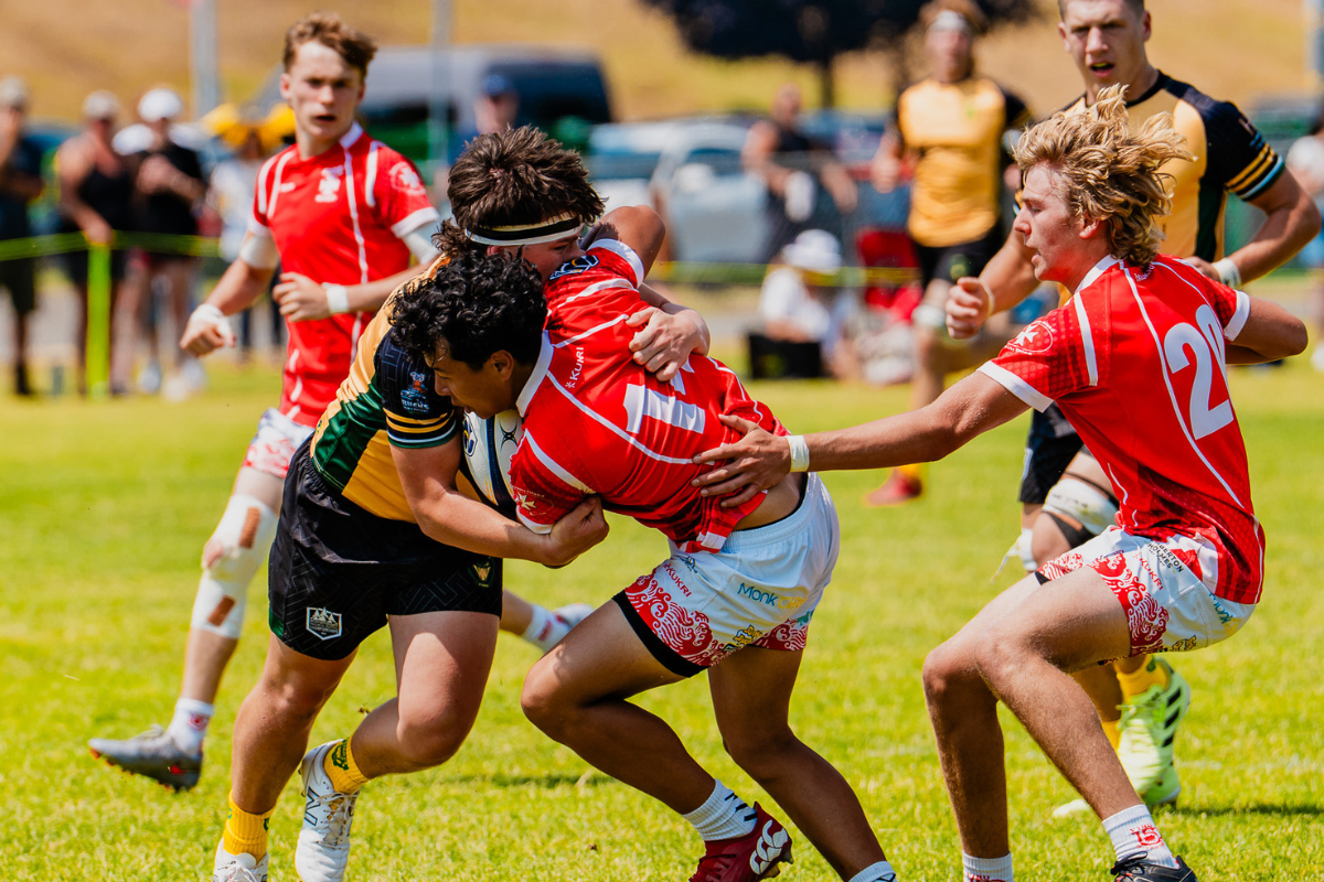 Rugby players in red tackle an opponent in black on a grassy field during a match