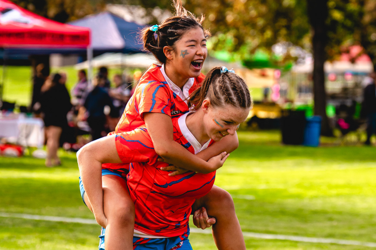 Two athletes in red uniforms sharing a piggyback ride on a grassy field during a sports event