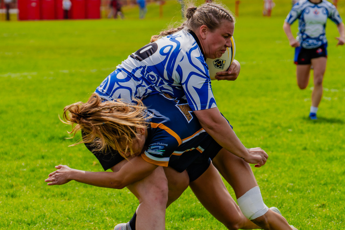 Two athletes in blue jerseys tackle on a grassy field during a rugby match