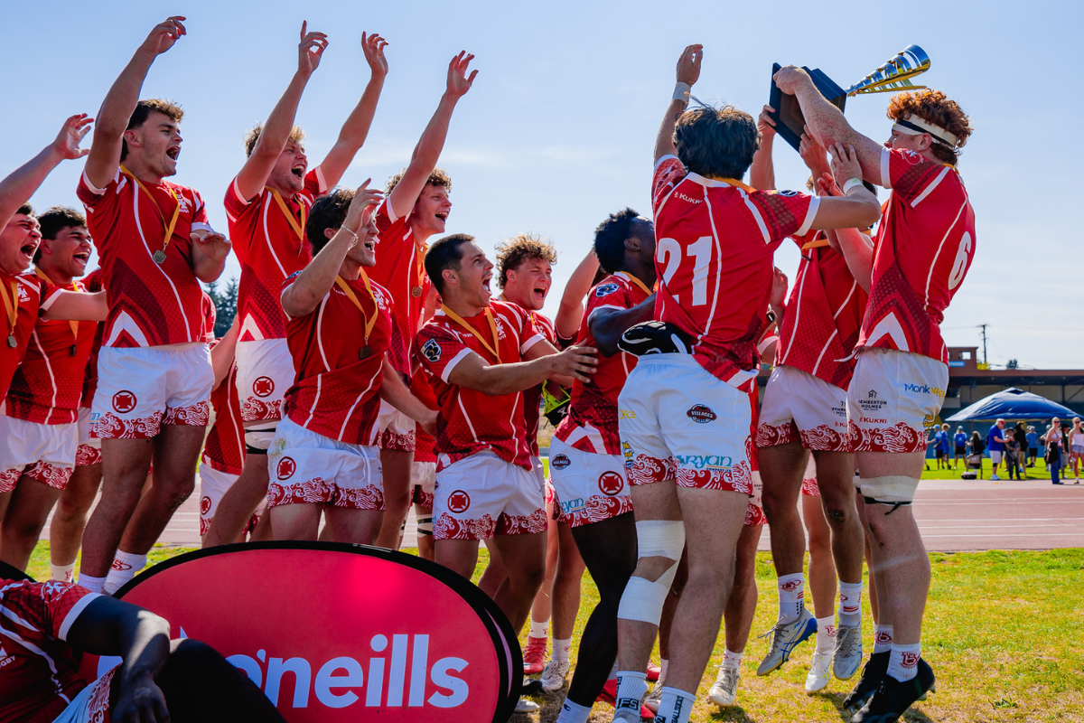 Red-uniformed team celebrating with trophy on a sports field under bright sun