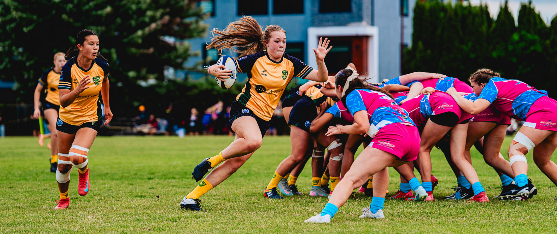Two teams playing rugby on a muddy field, one player running with the ball while others tackle