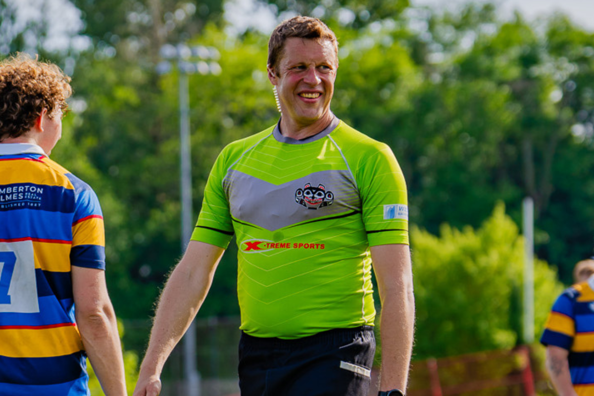 Two rugby players in striped jerseys outdoors, with one in a bright green shirt smiling at center