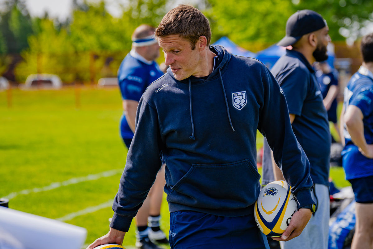 Rugby player in navy training gear holding a ball on a grassy field during practice