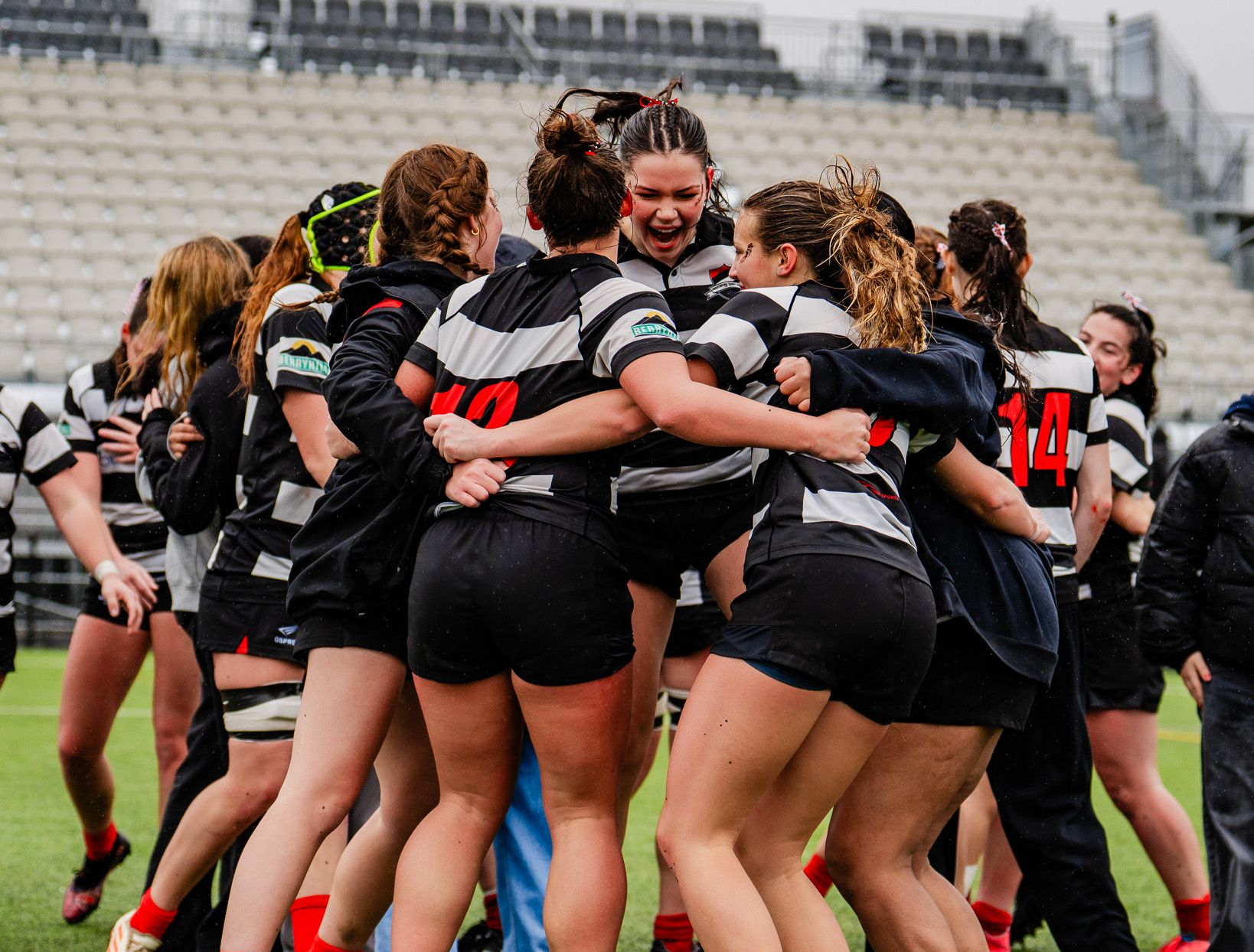 Women’s rugby team in black and white huddles and celebrates on the field after a play