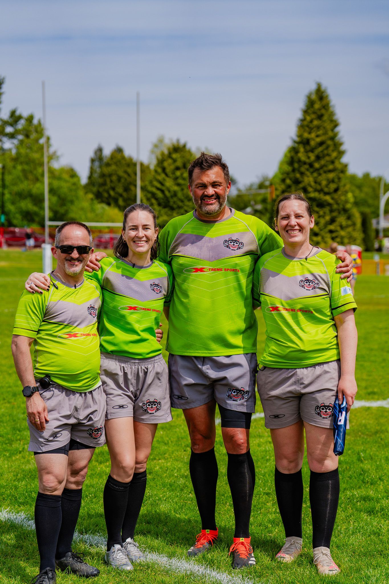 Four runners in neon green jerseys pose together on a grassy field outdoors.