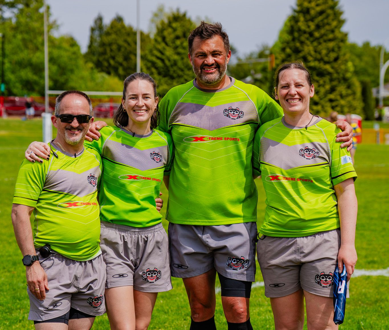 Four people in neon green sports jerseys pose together outdoors on a sunny day.