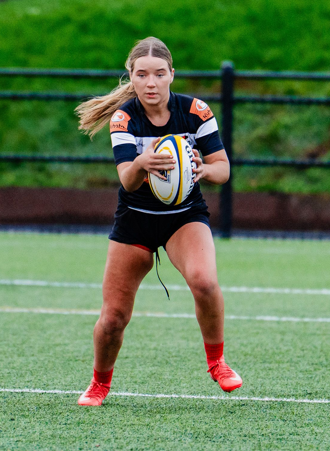 Rugby player in black and white uniform runs with the ball on a wet field