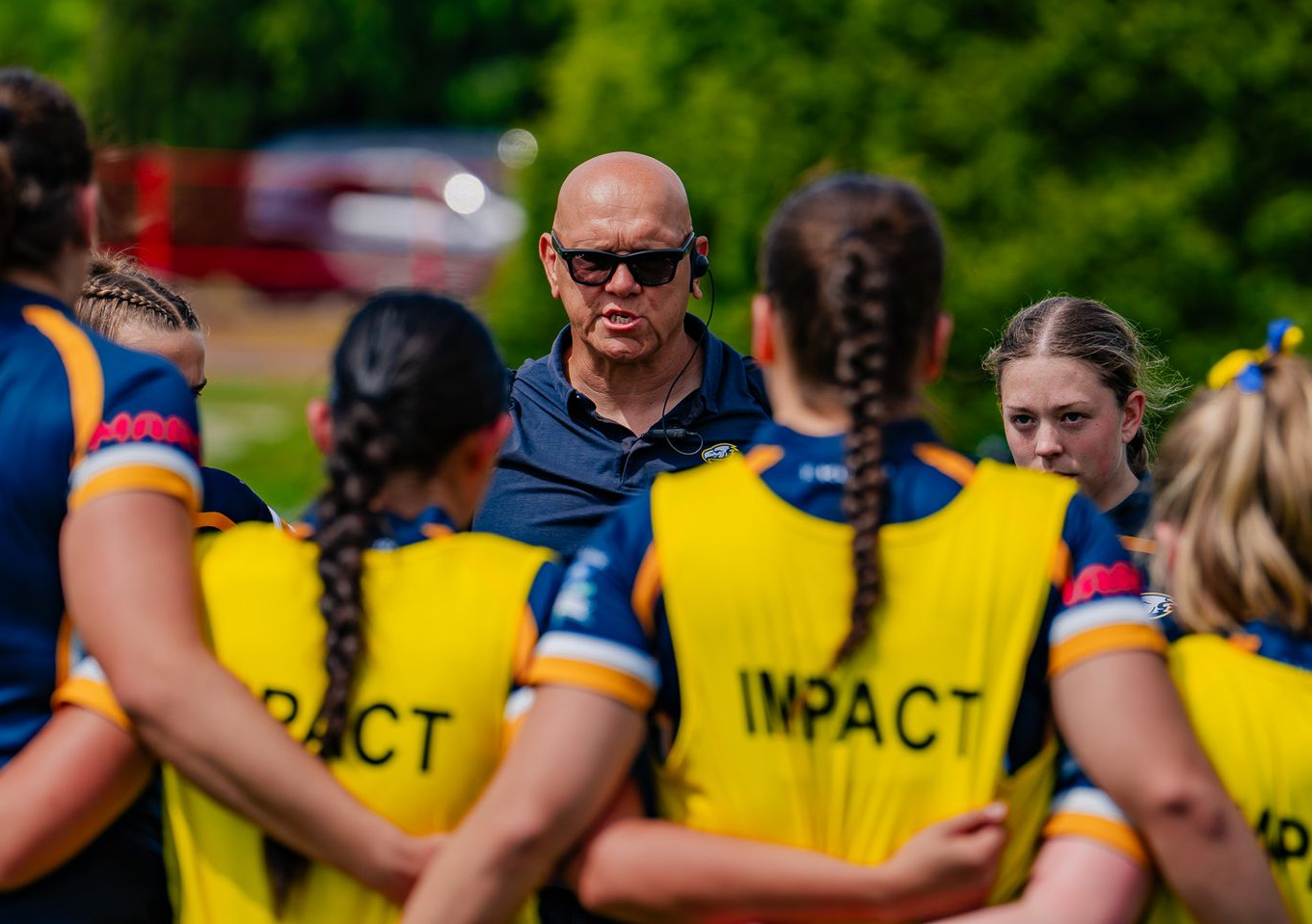 Coach speaking to a group of players in yellow jerseys on a field