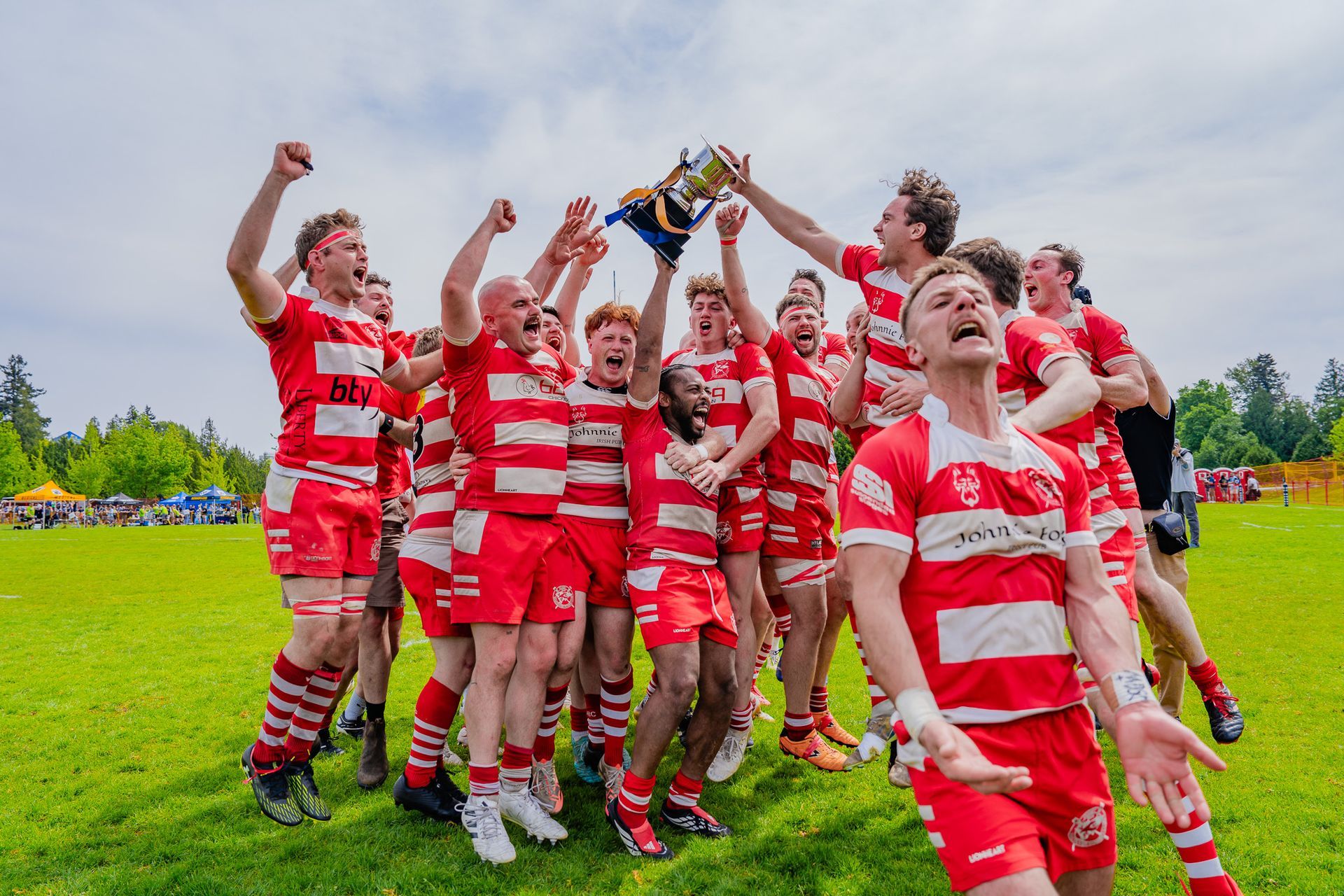 Red-and-white striped rugby team celebrating on a field, lifting a trophy overhead
