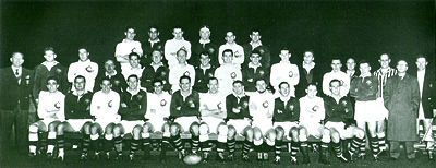 Black-and-white team portrait of a large group posed in rows indoors, some holding trophies.