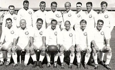 Black-and-white group portrait of a soccer team in white uniforms, posed in two rows with a ball in front
