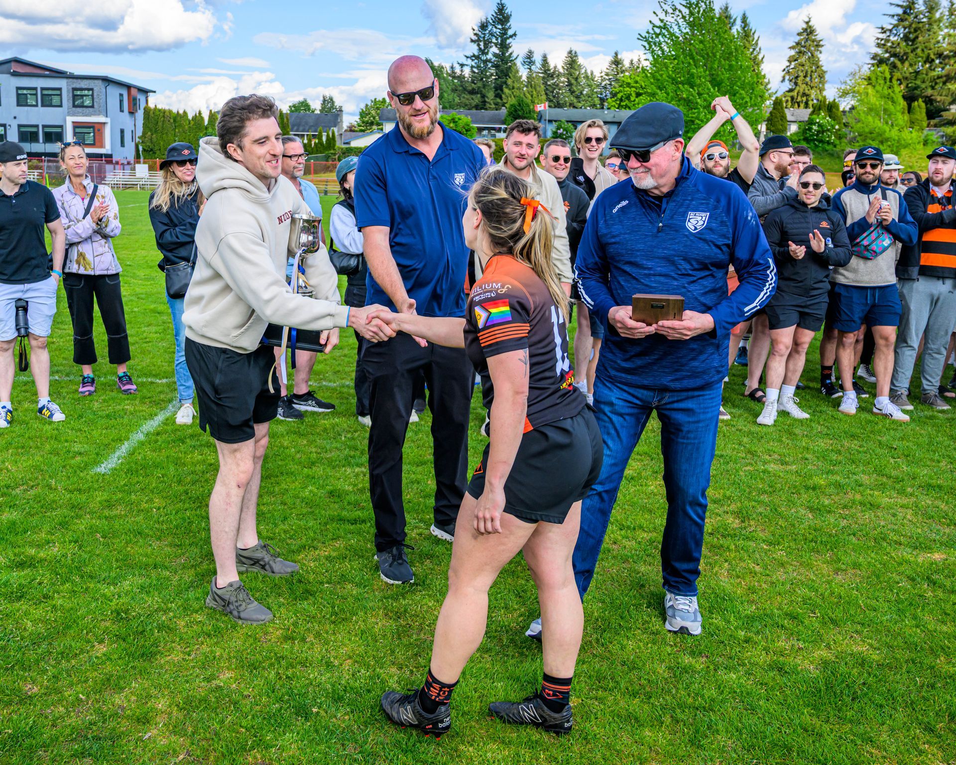 Woman receives an award on a grassy field as officials and a crowd watch nearby.