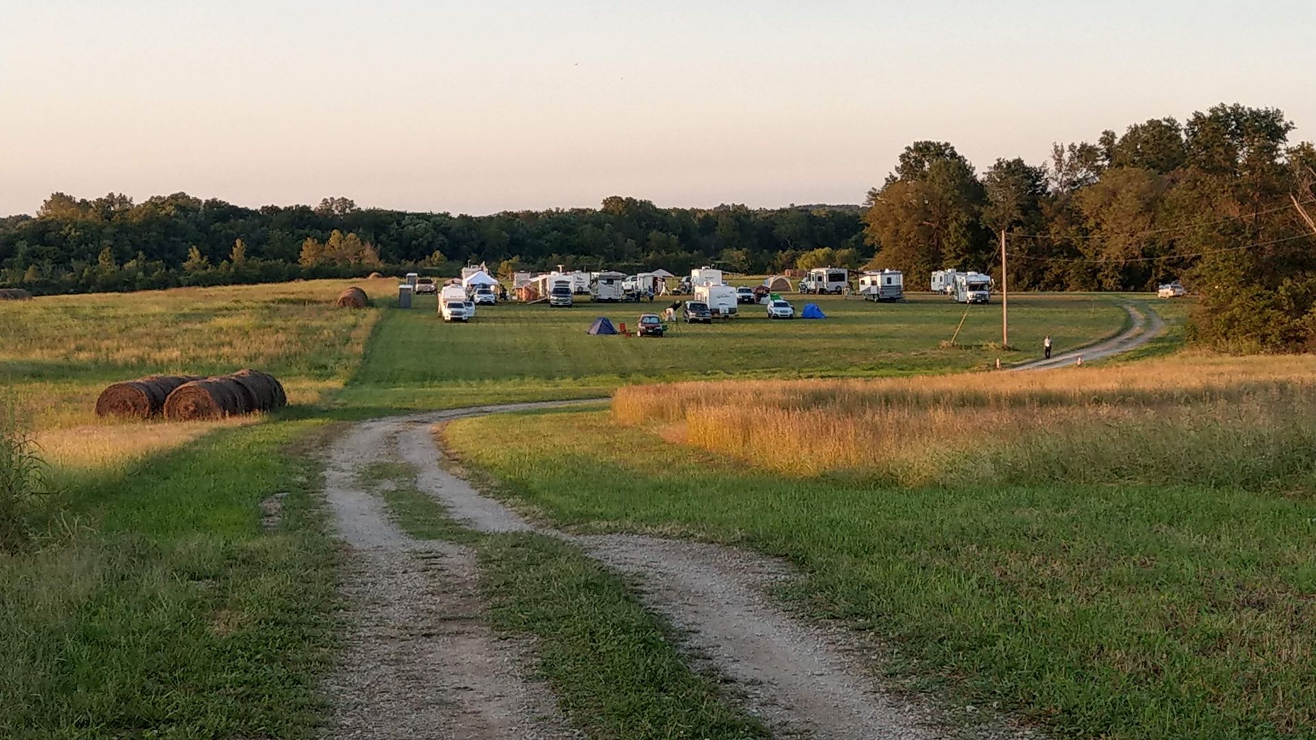 Gravel path through a grassy field toward a campsite with parked vehicles under a clear sky
