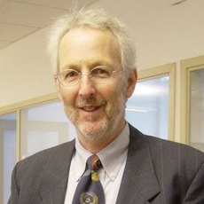 Smiling man in a gray suit and patterned tie standing in an office hallway