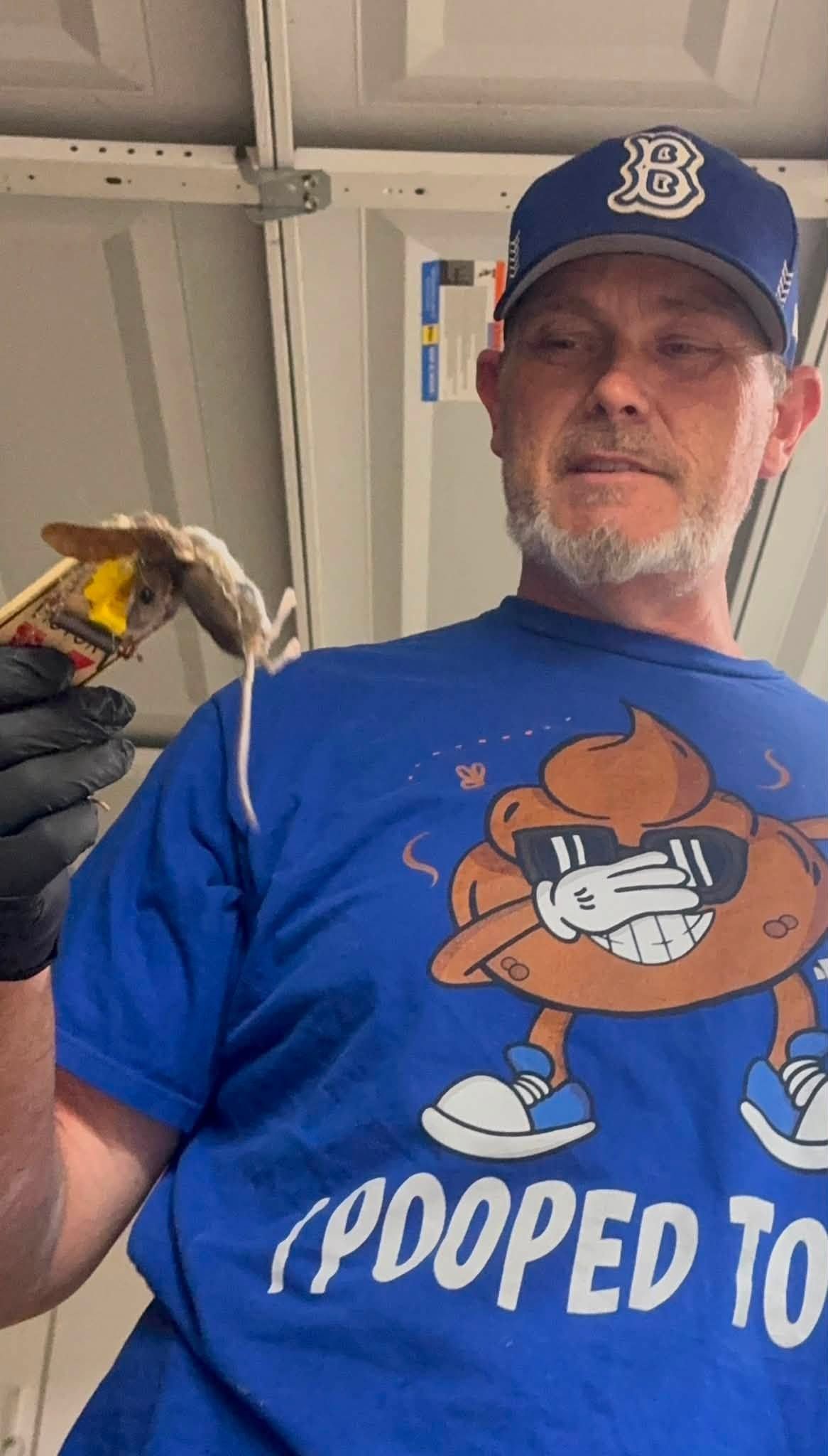 Man in blue shirt and cap holding a small bird indoors, with a cartoon graphic on his shirt.