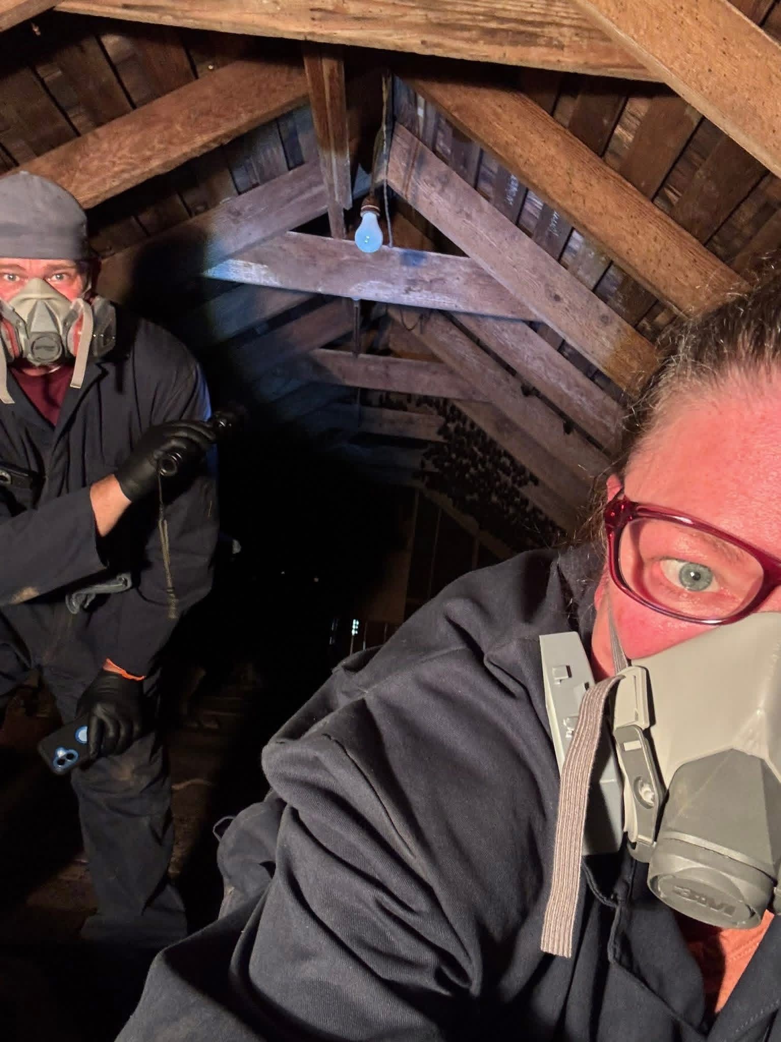 Two masked workers in hard hats inside a narrow wooden tunnel, with one close to the camera.
