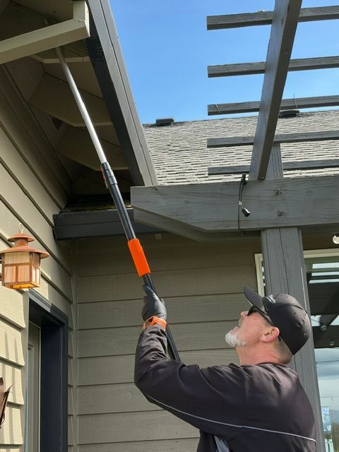 Worker using a long-handled tool to clean gutters under a house roof overhang