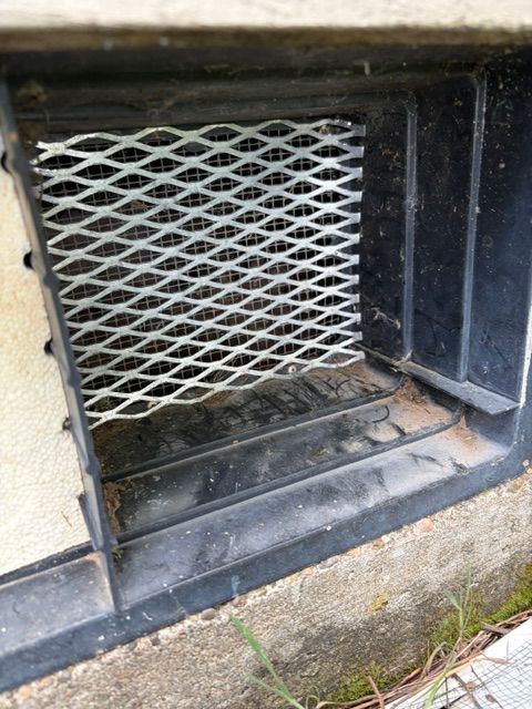 Metal basement vent with white lattice grate in a stone wall opening