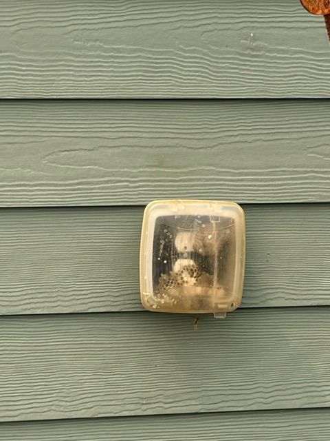 Weathered outdoor light fixture on green siding with a frosted cover