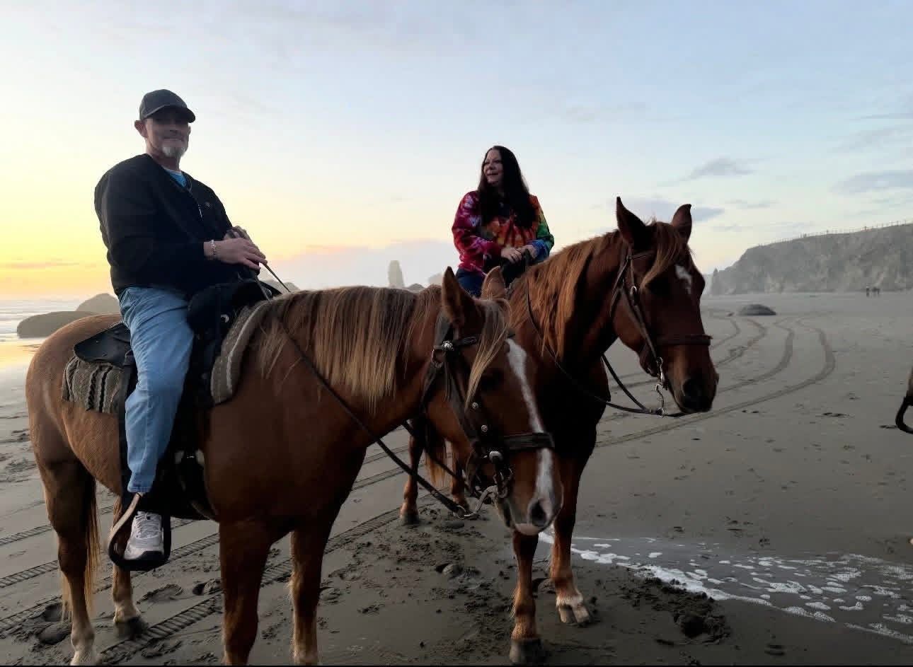 Two people riding horses on a sandy beach at sunset