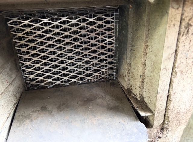 Closed metal vent with diamond-pattern grille inside a concrete opening