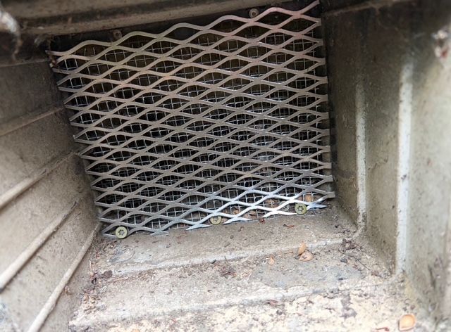 Dusty metal vent with diamond-pattern grille inside a small wall opening