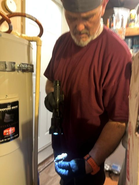 Man working on a water heater, using a flashlight in a utility room
