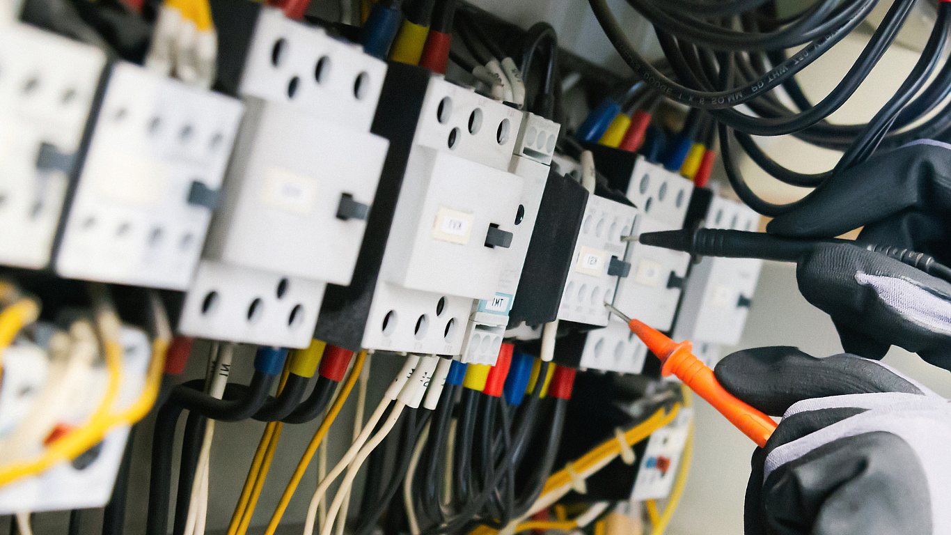 Electrical panel wiring with labeled breakers and a gloved hand using an orange screwdriver