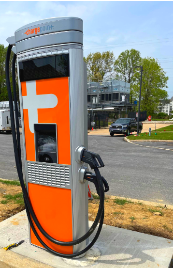 Orange public electric vehicle charging station with a plugged-in cable in a parking lot outdoors