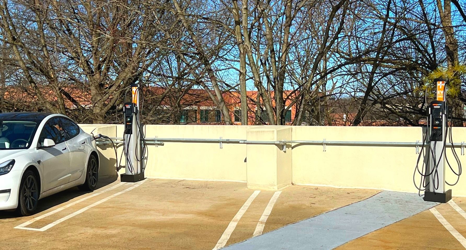 Parking lot with EV charging station, white car, and bare trees on a sunny day