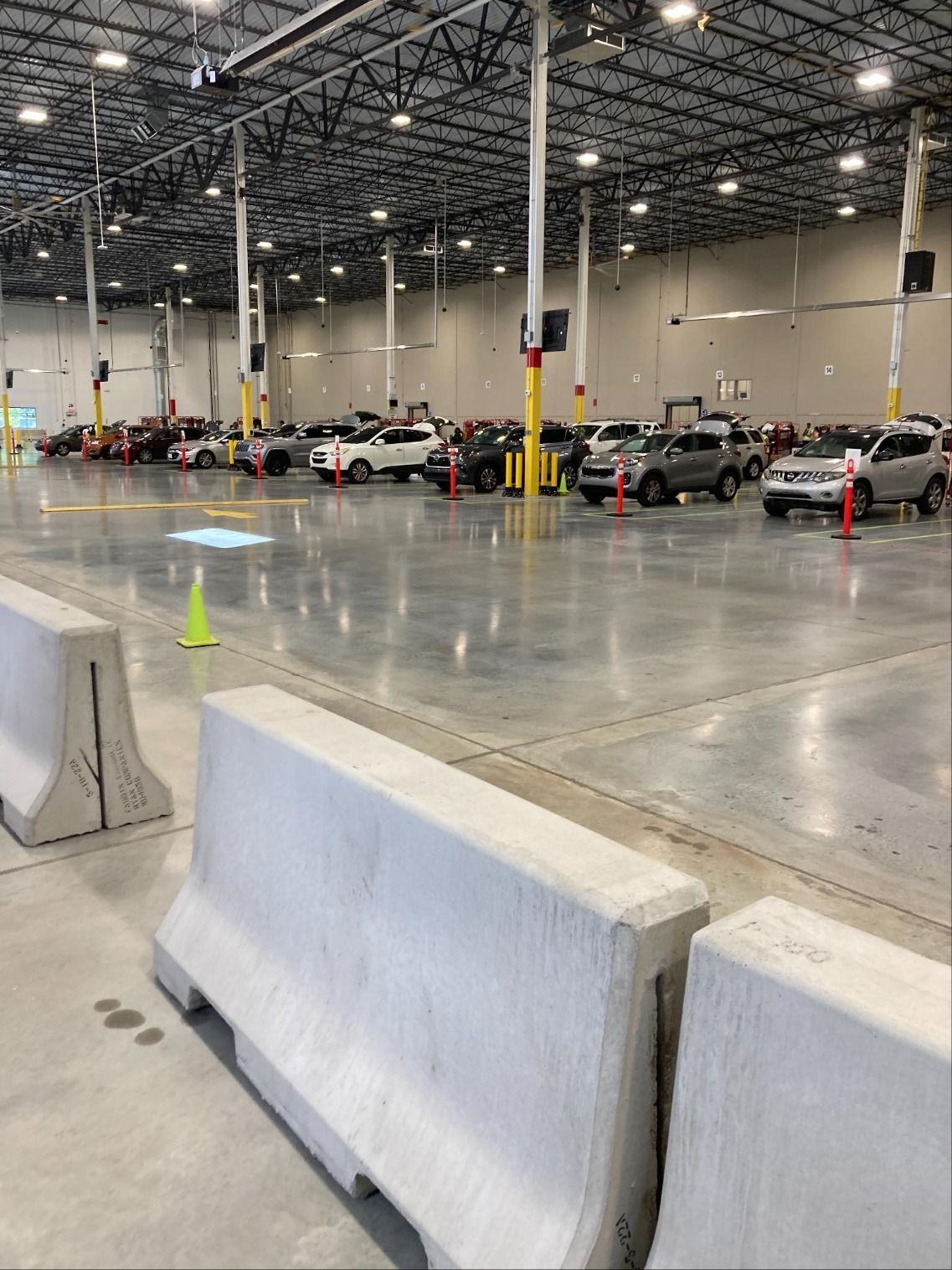 Indoor parking lot with concrete barriers, orange cones, and parked cars under bright industrial lighting