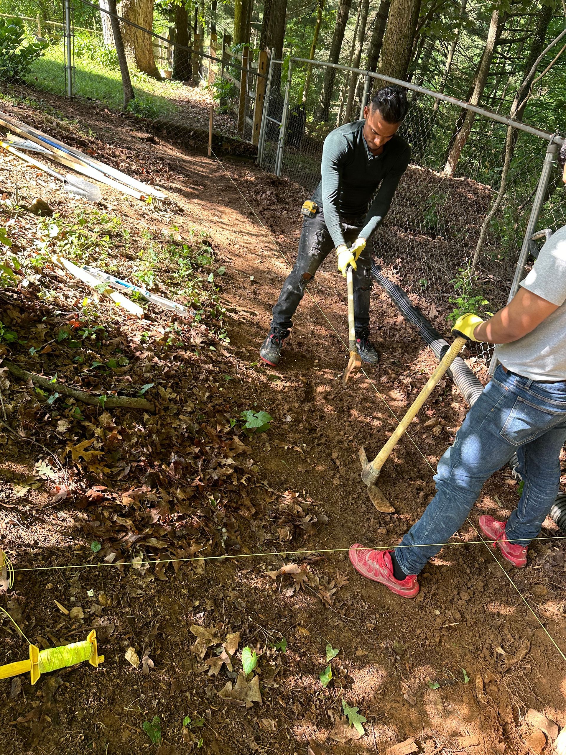 Two men are digging in the dirt with shovels and hammers.