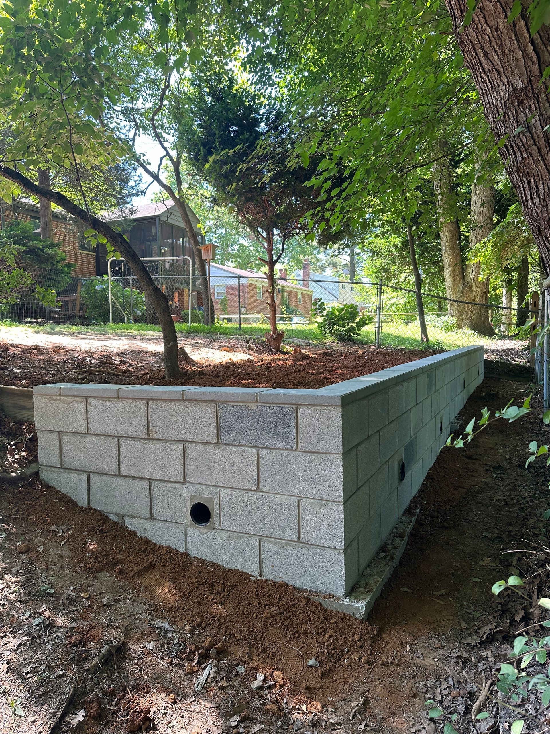 A concrete block wall is being built in a backyard next to a tree.