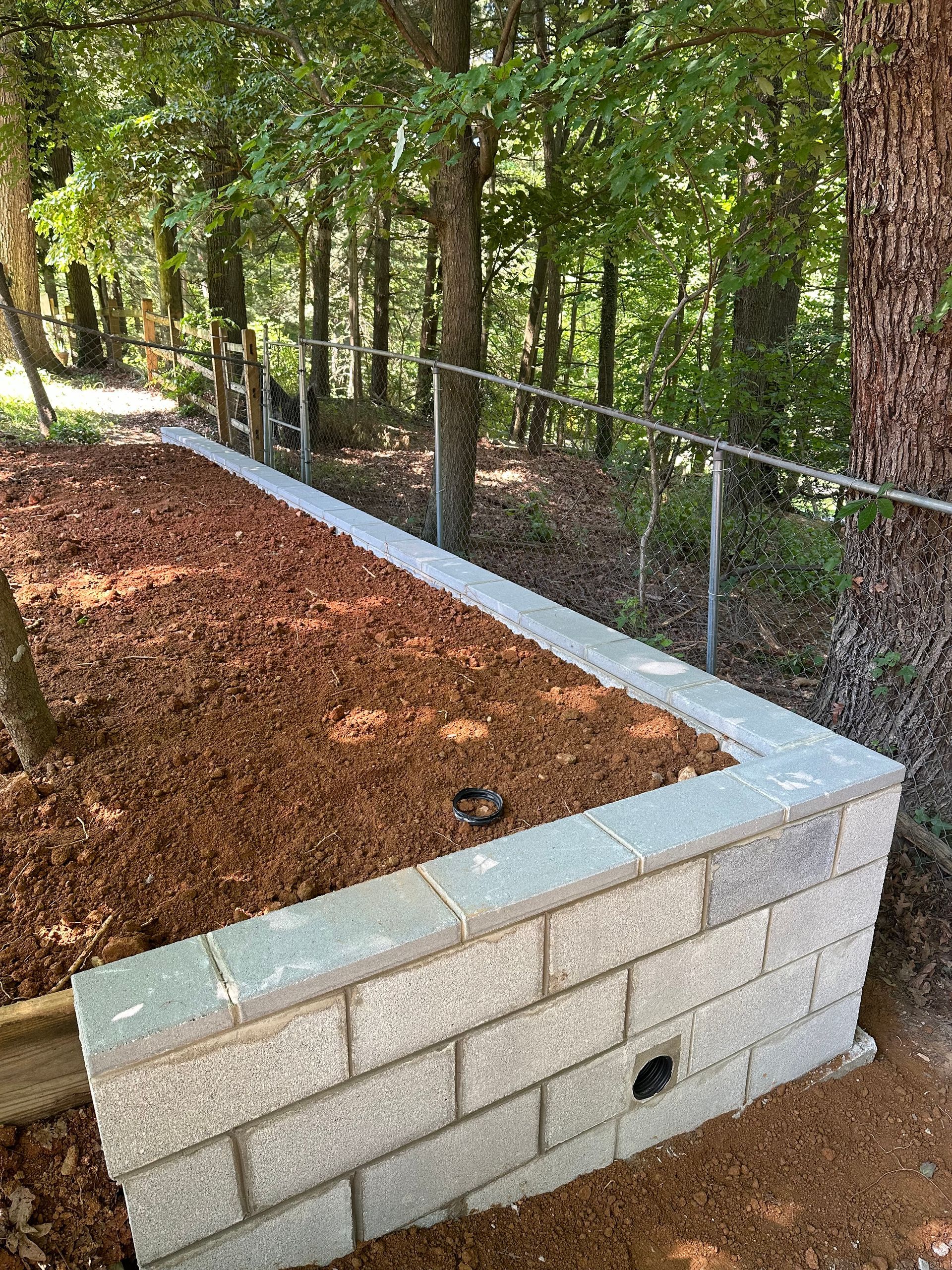 A concrete block wall ifilled with dirt next to a fence.