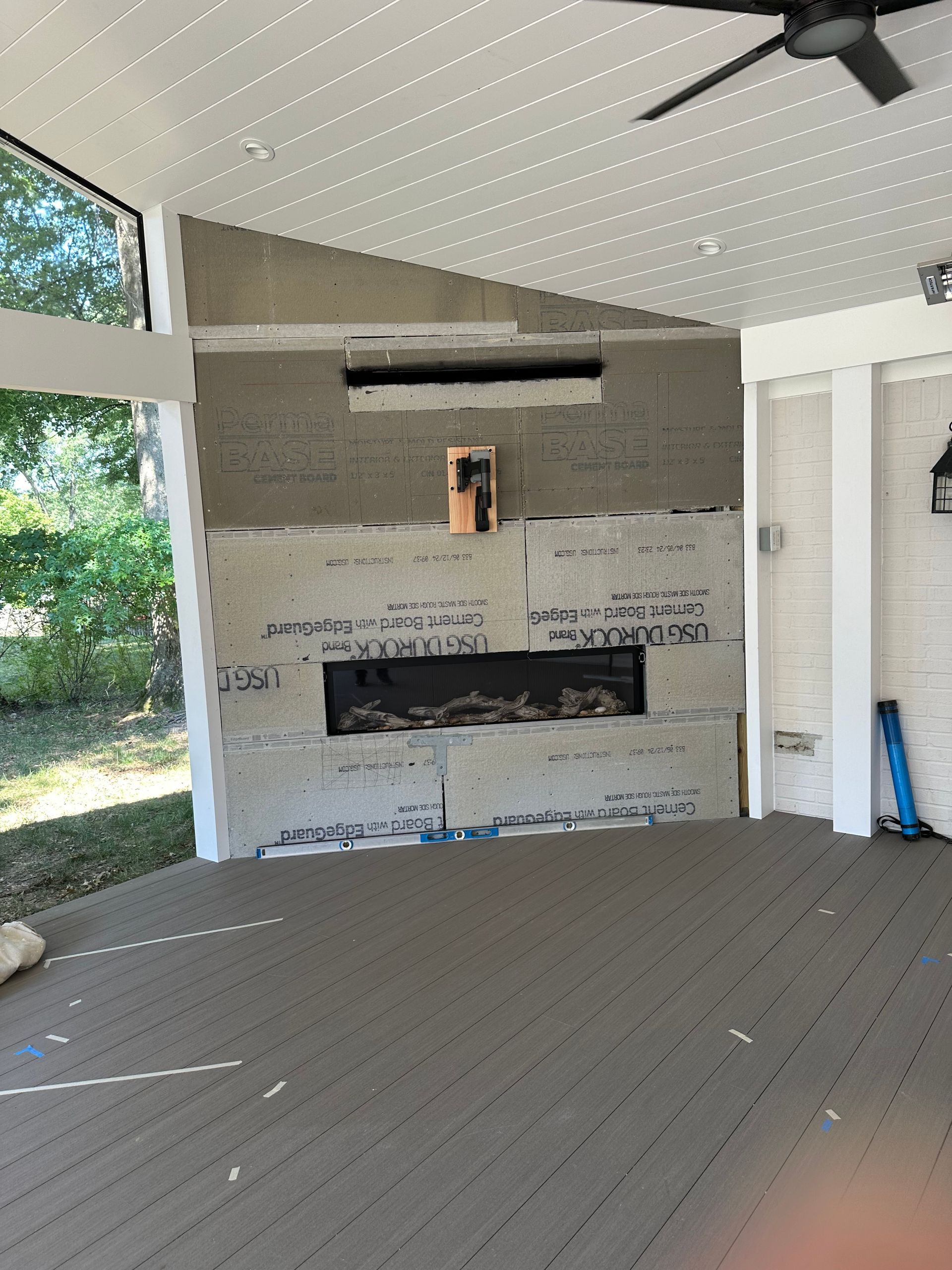 An empty room with a fireplace under installation and a ceiling fan.