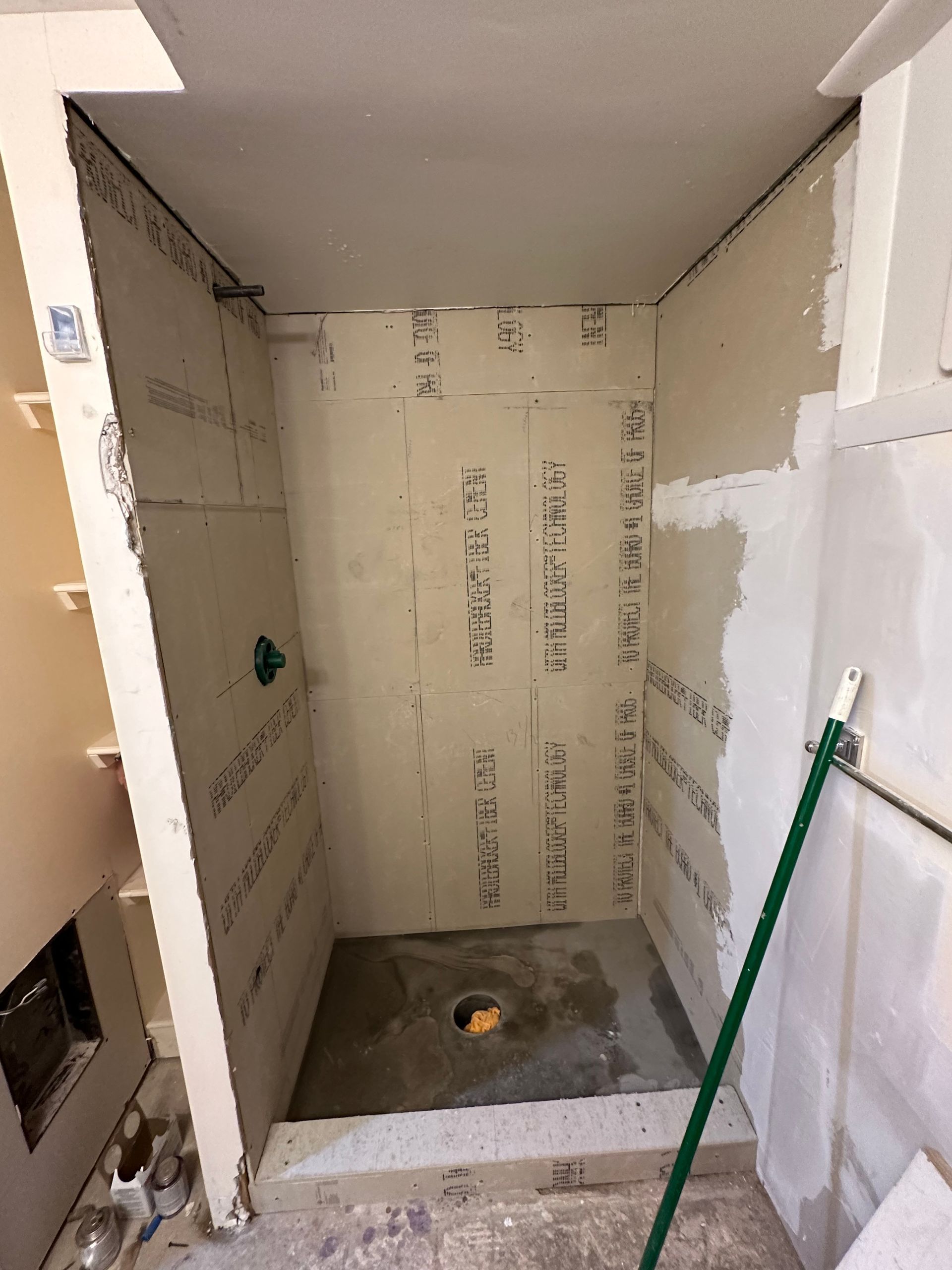 A bathroom under construction with a green broom in the corner