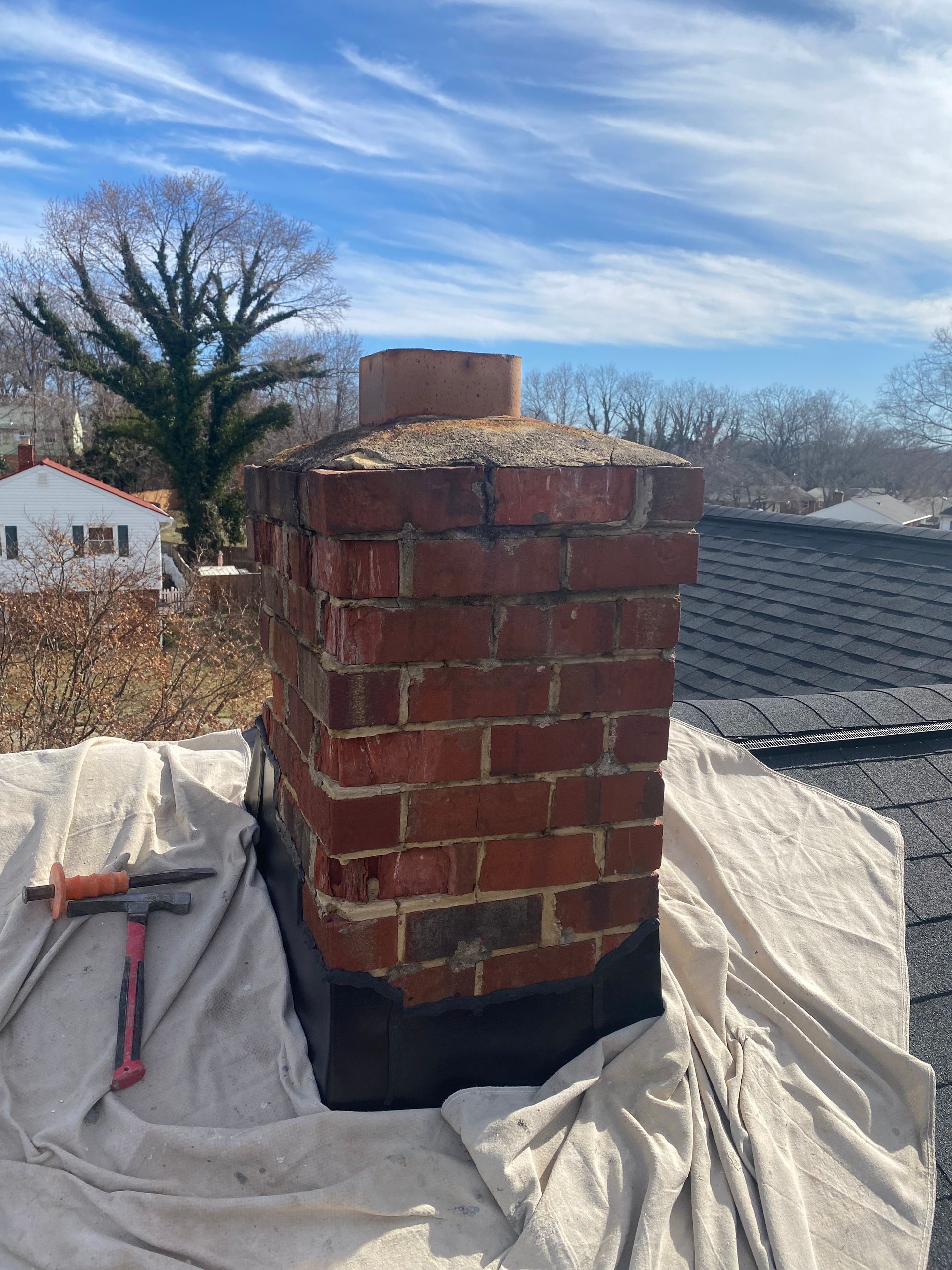 A brick chimney with a white cloth and tools on a roof.