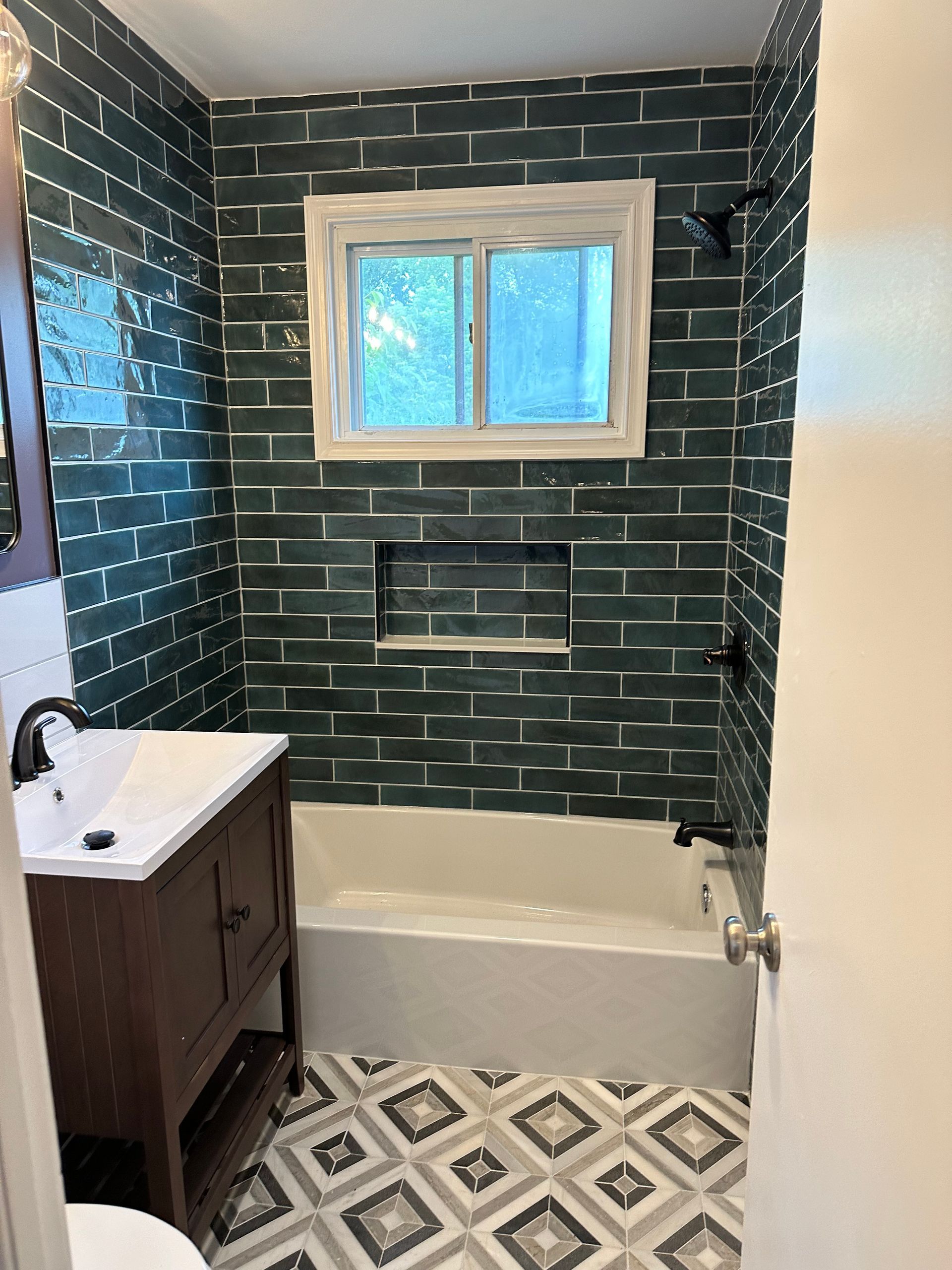 A remodeled bathroom with a sink , tub , mirror and window with beautiful tile work. .