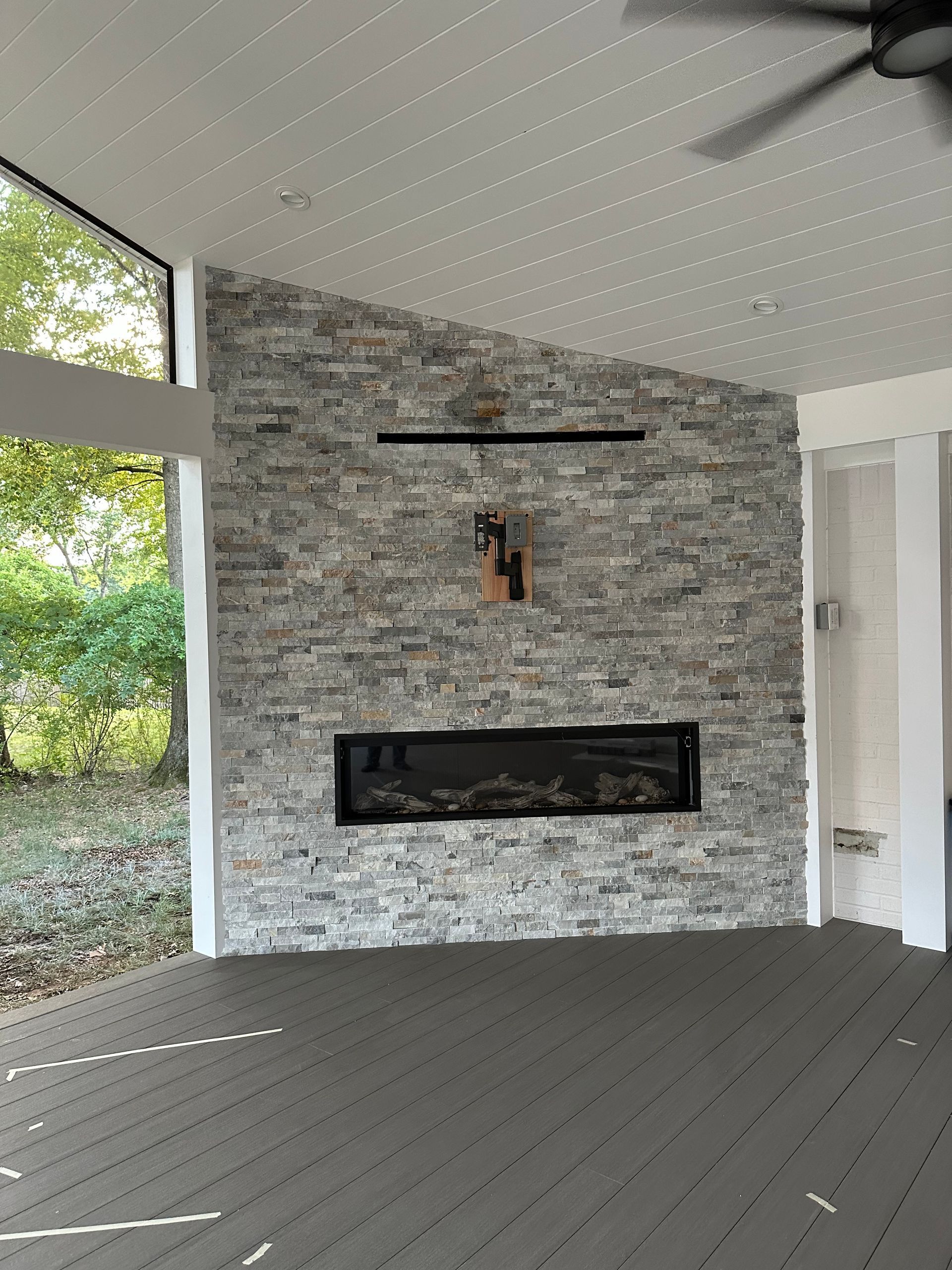 A living room with a fireplace  with stone veneer and a ceiling fan